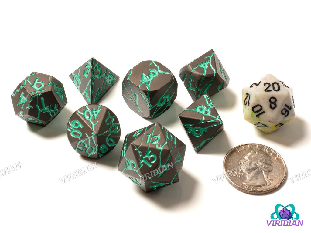 Colossus of Rhodes 7-piece metal dice set shown with a white D20 and quarter for size comparison, featuring cracked bronze and teal design.